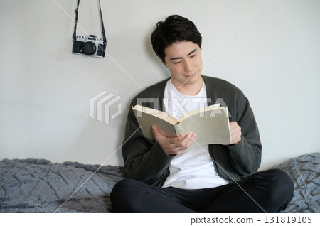 Man sitting on bed reading a book 131819105