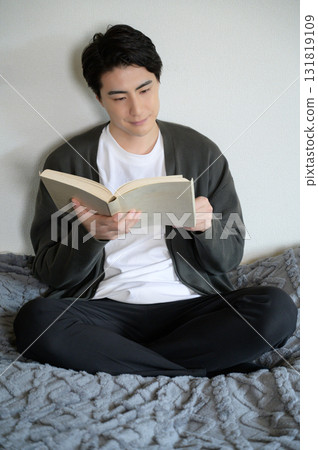 Man sitting on bed reading a book Man sitting on bed reading a book 131819109