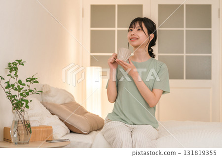 晚上，年輕的亞洲女子在臥室喝熱飲 131819355