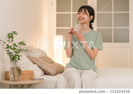 Young Asian woman drinking a hot drink in her bedroom at night 131819356