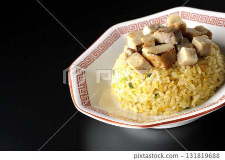 Egg fried rice topped with diced pork slices photographed against a black background 131819688