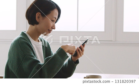 A woman in her 40s smiling and looking at her mobile phone screen 131820397