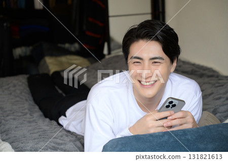 A man lying face down on the bed operating a smartphone A man lying face down on the bed operating a smartphone 131821613