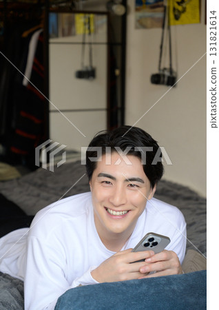 A man lying face down on the bed operating a smartphone A man lying face down on the bed operating a smartphone 131821614