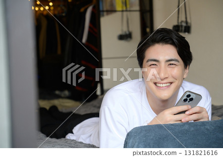 一名男子趴在床上操作智慧型手機 一名男子趴在床上操作智慧型手機 131821616