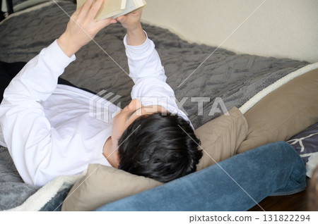 A Japanese man lying on his back reading a book 131822294