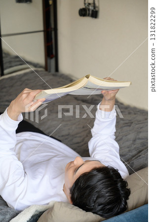 A Japanese man lying on his back reading a book 131822299