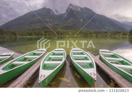 Green rowboats moored to wooden docks on clear mountain lake with forest and peaks in background 131828623