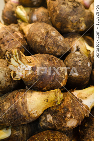 Fresh taro roots stacked together at a local market, showcasing their earthy textures and vibrant skin during a busy morning in a tropical region Fresh taro roots stacked together at a local market, showcasing their earthy textures and vibrant skin during a busy morning in a tropical region 131828758