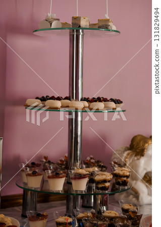 Elegant Three-Tier Dessert Stand Display with Mini Pastries and Fruit on Pink Background, Luxury Confectionery Showcase. Elegant Three-Tier Dessert Stand Display with Mini Pastries and Fruit on Pink Background, Luxury Confectionery Showcase. 131829494