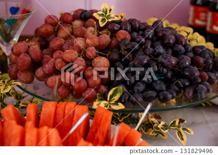 Fresh Fruit Platter Display with Red and Purple Grapes, Watermelon, and Greenery on Glass Plate 131829496