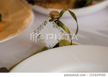 Elegant Wedding Favor Bottle with Floral Tag, Olive Oil, White Plates, Soft Focus Table Setting, Green and Beige Color Palette. Elegant Wedding Favor Bottle with Floral Tag, Olive Oil, White Plates, Soft Focus Table Setting, Green and Beige Color Palette. 131829500