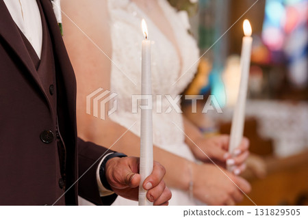Orthodox Wedding Ceremony Candles Lighting with Bride and Groom in Church, Warm Tone, Traditional Celebration, Rich Burgundy Detail. Orthodox Wedding Ceremony Candles Lighting with Bride and Groom in Church, Warm Tone, Traditional Celebration, Rich Burgundy Detail. 131829505