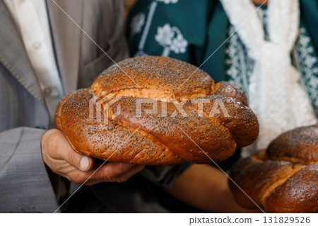 Traditional Jewish Wedding Challah Bread Ceremony, Groom and Bride Holding Poppy Seed Loaf, Rustic Texture, Warm Lighting Traditional Jewish Wedding Challah Bread Ceremony, Groom and Bride Holding Poppy Seed Loaf, Rustic Texture, Warm Lighting 131829526