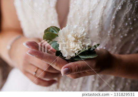Elegant Bride Holding White Carnation Boutonniere with Eucalyptus, Close-Up Wedding Florals, Pearl Gown Detail. Elegant Bride Holding White Carnation Boutonniere with Eucalyptus, Close-Up Wedding Florals, Pearl Gown Detail. 131829531