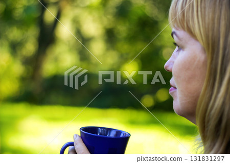 a cozy, relaxing moment of a woman enjoying a hot drink tea beverage outside, with a close-up focus on the mug. cozy woman hot drink sip ceramic cup blurred nature background lifestyle 131831297