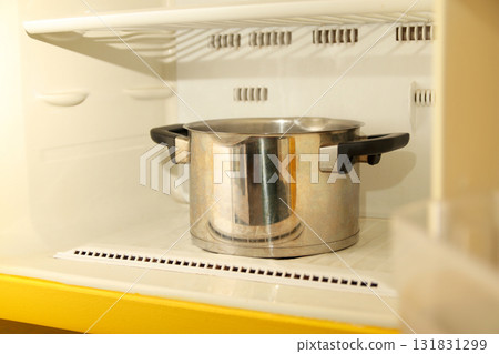 a frozen freezer or refrigerator compartment with thick layers of ice, using a saucepan of boiling water inside to melt the frost 131831299