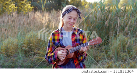 cute girl playing acoustic ukulele guitar outside grass happy portrait. a happy, young girl playing an acoustic guitar or ukulele outside on the grass to convey music, fun, and a cute lifestyle cute girl playing acoustic ukulele guitar outside grass happy portrait. a happy, young girl playing an acoustic guitar or ukulele outside on the grass to convey music, fun, and a cute lifestyle 131831304