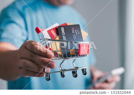 Hand holding shopping cart filled with credit cards retail store e-commerce indoor close-up view consumerism 131832044