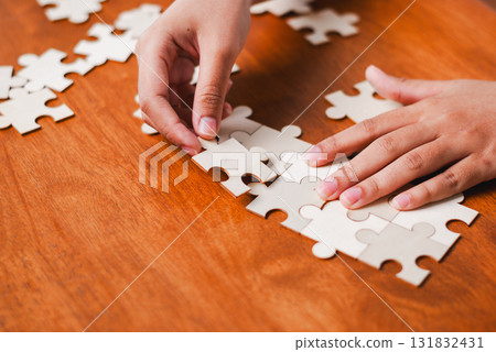 Puzzle solving activity at home engaging hands with unfinished pieces wooden table 131832431