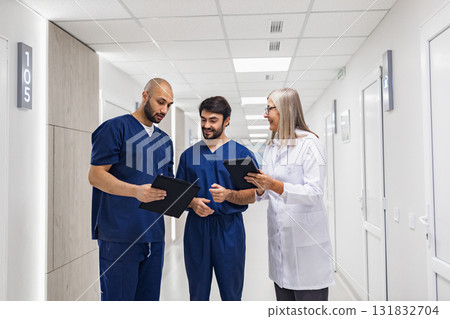 A doctor and two nurses are reviewing medical records in a clinic hallway, discussing patient care. A doctor and two nurses are reviewing medical records in a clinic hallway, discussing patient care. 131832704
