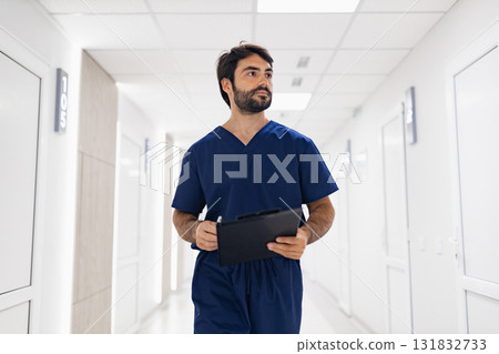 A doctor in scrubs walks down a bright hallway, holding a clipboard, likely heading to see a patient. A doctor in scrubs walks down a bright hallway, holding a clipboard, likely heading to see a patient. 131832733