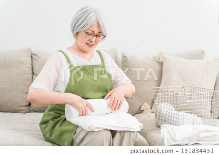 Senior Asian woman folding laundry in the living room at home (housework, housewife, full-time housewife) 131834431