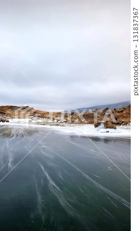 Frozen Lake Baikal shore with smooth ice leading to rocky brown hills Frozen Lake Baikal shore with smooth ice leading to rocky brown hills 131837367