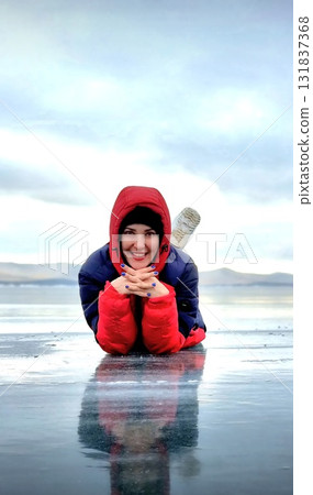Woman lying down smiling on the smooth, cold ice of Lake Baikal 131837368