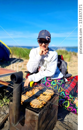 Woman smiling happily while grilling food at a sunny beachside camp Woman smiling happily while grilling food at a sunny beachside camp 131837371