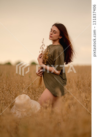 Woman in a field holding wheat and oats while enjoying a serene moment outdoors 131837406