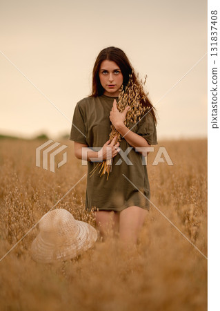Woman standing in an oat field holding wheat stalks during sunset Woman standing in an oat field holding wheat stalks during sunset 131837408