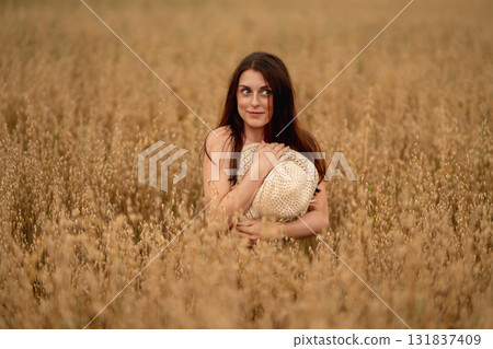 Young woman enjoying a sunny day in a field of oats and wheat, holding a straw hat Young woman enjoying a sunny day in a field of oats and wheat, holding a straw hat 131837409