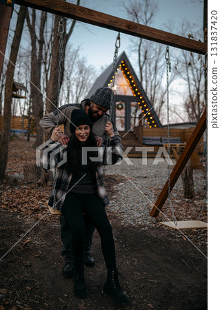 Couple enjoying a playful moment on swings near cozy cabin during twilight 131837420