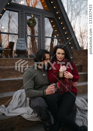 Couple enjoying a cozy moment on wooden steps outside a modern cabin during winter 131837435