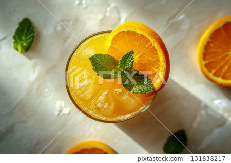 A vibrant orange drink sits on a light surface, garnished with fresh mint and a slice of orange, capturing a warm afternoon atmosphere 131838217
