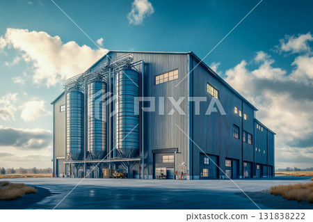 A large grain storage facility features tall silos, set against a backdrop of open fields under a bright blue sky A large grain storage facility features tall silos, set against a backdrop of open fields under a bright blue sky 131838222