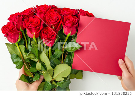 A vibrant bouquet of red roses is held by hands alongside a blank red card, ready for gifting on a special occasion 131838235