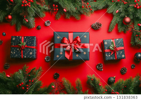Brightly wrapped gifts sit on a vivid red surface, surrounded by pine branches and ornaments, creating a cheerful holiday scene 131838363