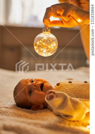 Newborn baby in a knit romper lies on a cozy blanket, gazing up in wonder at a clear Christmas 131838664