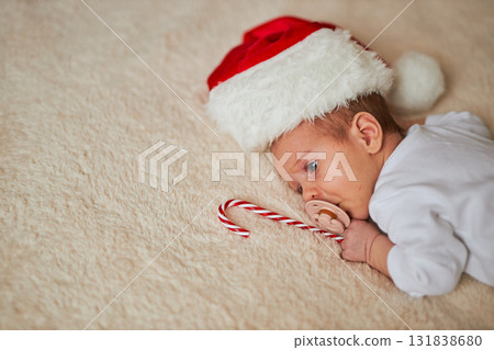 A close-up of a newborn baby in a white onesie, lying on its tummy on a fluffy beige blanket. The A close-up of a newborn baby in a white onesie, lying on its tummy on a fluffy beige blanket. The 131838680