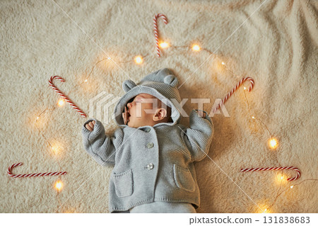 A newborn baby in a gray knit hooded outfit with bear ears is peacefully sleeping, surrounded by 131838683