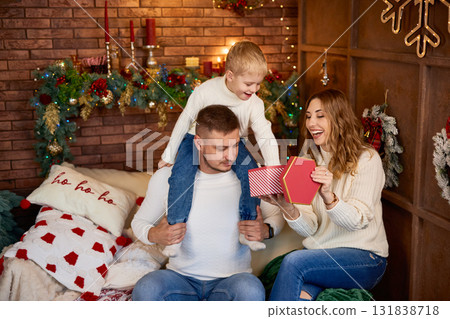 Happy family in white sweaters exchanging a Christmas gift in a cozy loft-style room with a brick 131838718
