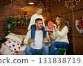 Happy family in white sweaters exchanging a Christmas gift in a cozy loft-style room with a brick 131838719