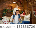 Happy family in white sweaters exchanging a Christmas gift in a cozy loft-style room with a brick 131838720
