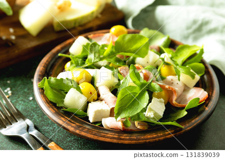 Fresh arugula salad with prosciutto, melon, and olives for a delicious summer meal Fresh arugula salad with prosciutto, melon, and olives for a delicious summer meal 131839039