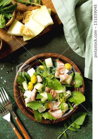 Fresh arugula salad with prosciutto, melon, and olives for a delicious summer meal. Top view flat lay 131839048
