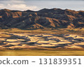 A stunning desert landscape showcasing rolling dunes against rugged mountains 131839351