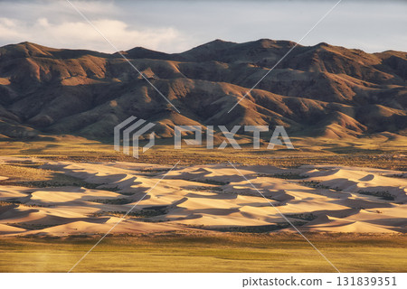 A stunning desert landscape showcasing rolling dunes against rugged mountains 131839351