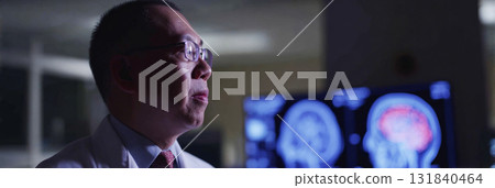 Focused doctor in a white coat with glasses stands in a dim hospital diagnostics room, intently examining information displayed on a digital screen, banner Focused doctor in a white coat with glasses stands in a dim hospital diagnostics room, intently examining information displayed on a digital screen, banner 131840464